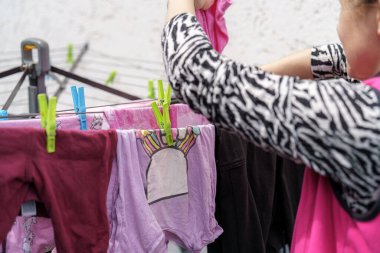 Uzun kollu gömlekli bir kadın çamaşır ipine çeşitli çamaşırları dikkatlice asıyor..