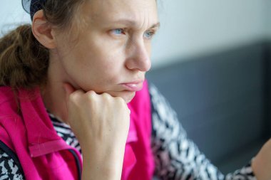 Bir kadın düşünceli bir şekilde parlak bir odada oturur, çenesini elinin üzerine koyar. Onun ifadesi tefekkür ve merakı yansıtır. İçerideki rahat alan atmosferi güçlendirir..