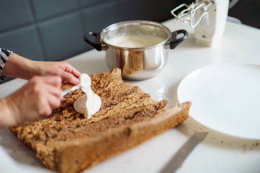 Eller, ahşap bir yüzeyde, krema kasesi ve mikseri modern bir mutfak ortamında olan bir tatlıya dikkatlice krema sürüyor. Gündüz vakti gibi görünüyor..
