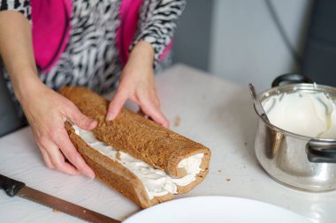 Bir fırıncı, güneşli bir öğleden sonra sıcak bir mutfakta, kremayla dolu yeni pişmiş bir sünger keki ustalıkla sarar..