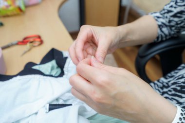 El işi masasında elbise dikmeye odaklanmış bir insan. Çalışma alanında makas ve kumaş kalıntıları var. Etkinlik, terzilik ve yaratıcılık sanatını vurguluyor.