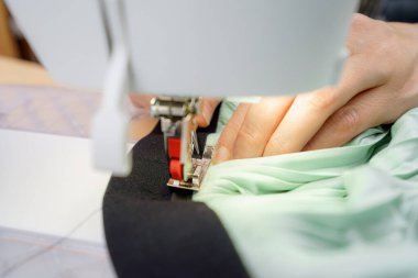 El sanatları ustası bir dikiş makinesi kullanıyor. Nane yeşili bir kumaşı, rahat bir atölyedeki siyah kumaş tabanına ustalıkla dikiyor. Odaklanma hassasiyet ve detaydır..