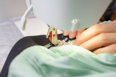 Eller ustalıkla bir kumaş parçasını iyi aydınlatılmış bir çalışma alanındaki dikiş makinesinin iğnesinin altına yerleştirdi. Dikiş süreci karmaşık ayrıntıları ve yaratıcılığı sergiler.