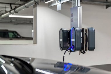Gösterişli bir elektrikli araç şarj istasyonu iyi aydınlatılmış bir yeraltı otoparkının duvarına monte edilir. Şarj kabloları sarkıyor, elektrikli arabaların kullanımına hazır..