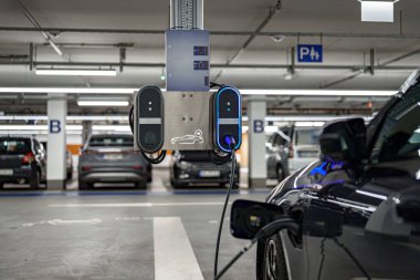 Geniş bir yeraltı otoparkına elektrikli araç şarj istasyonu kuruldu. Şarj kablosu olan birden fazla araba, modern altyapıyı sergilemek için yakınlarda park halinde..