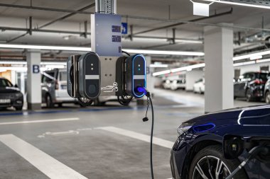 İşçiler, işlek bir yeraltı otoparkındaki son model elektrikli taşıt şarj istasyonunun bakımını üstleniyorlar..