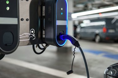 Elektrikli bir araç bir şarj istasyonuna bağlı, parlak tasarım ve teknolojiyi sergiliyor. Park alanı iyi ışıklandırılmış ve şarj için kolay erişim için tasarlanmış..