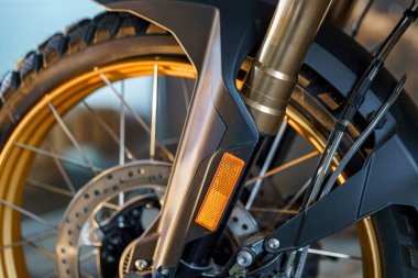 Bu yakın çekim bir motorsikletin ön çatalının karmaşık dizaynını yakalar. Odak, iyi aydınlatılmış bir atölye ortamında süspansiyon sistemi, lastik izi ve metalik bileşenleri vurgular.