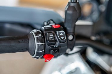 Motosiklet gidon kontrollerinin kapatılması, arka planda araçları olan bir atölye ayarında yer alan ve menü navigasyon ve ayarlama için kullanılan çeşitli düğmeleri ortaya çıkarır.