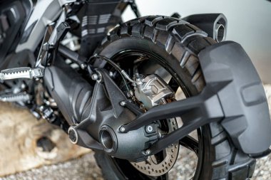 Bu yakın çekim bir motosikletin arka tekerleğini gösteriyor, ayrıntılı fren sistemini ve süspansiyon mekaniklerini vurguluyor. Kentsel arkaplan sahneye bağlam ekler.