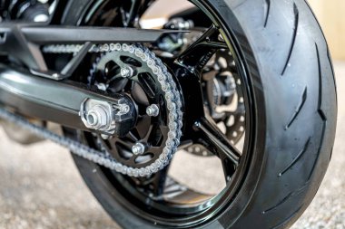 Görüntü, parlak bir zincire ve roket sistemine sahip bir motosikletin arka tekerleğinin detaylı bir yakın çekimini çeker. Güneşli bir öğleden sonra, karmaşık lastik lastik izi tasarımına vurgu yapar..