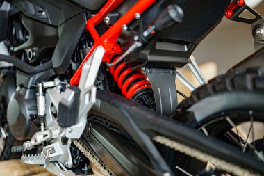 Kırmızı yay ve çeşitli mekanik parçaları gösteren bir motosikletin süspansiyonuna karmaşık bir bakış. Ayar, motosiklet bakımına olan tutkusunu yansıtan, yakınlarda aletleri olan bir garaj gösteriyor..