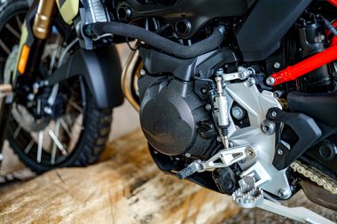 Motosiklet motorunun yakından incelenmesi vites kutusu, çerçeve ve egzoz bağlantıları da dahil olmak üzere karmaşık kısımları vurgular. Gösterişli tasarım bir atölyede hem işlevselliği hem de stili vurgular.