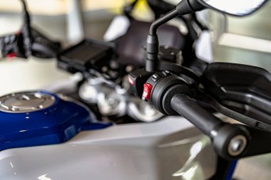 Motosiklet kontrollerinin, düğme ve kabzaları gösteren yakın çekim görüntüsü. Parlak garaj ayarı motorun özelliklerini ön plana çıkarıyor. Motosiklet tasarımı meraklıları ve tamirciler için mükemmel..