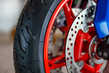 Bir motosiklet tekerleği belirgin bir şekilde parlak kırmızı teller ve gümüş bir fren diski ile sergilenir. Bu yakın çekim, iyi aydınlatılmış bir garaj ortamında karmaşık tasarım ayrıntılarını yakalar..