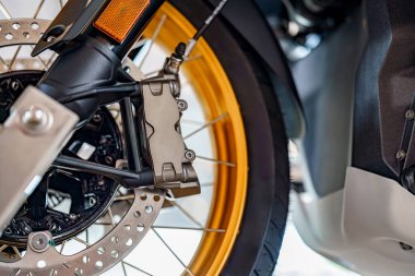 Bir motorsikletin fren kalibrelerine ve diskine odaklanın, iyi aydınlatılmış bir atölye ortamında altın kenarları ve karmaşık kısımları vurgulayın, işçiliği ve tasarımı vurgulayın.