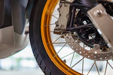 Motosiklet tekerleğinin, çarpıcı bir altın çember ve detaylı fren sistemini gösteren yakın görüntüsü, rutin bakım sırasında iyi aydınlatılmış bir garaj ortamında çekildi..