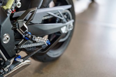 Gösterişli bir motosiklet ayaklığı ve vites kolu iyi aydınlatılmış bir galeride sergileniyor. Tasarım, performans ve estetiğin vurgulandığı modern materyal ve mühendisliği içeriyor..