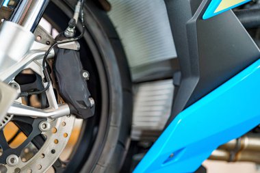 Motosiklet fren sisteminin karmaşık tasarımı, gümüş fren kalibreleri ve koyu tekerleklere odaklanarak vurgulanır. Bu, performans ve estetiğin kaynaşmasını gösteriyor..