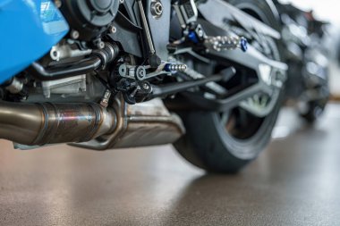 Motosikletin egzoz sisteminin detaylı yakın plan çekimleri yenilikçi tasarım ve mühendisliğini iyi aydınlatılmış bir galeride sergiliyor. Karmaşık kısımlara odaklanıldığında aracın kalitesi vurgulanır.