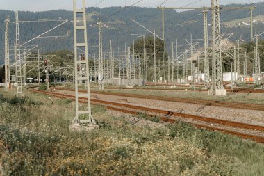 Gün batımında berrak bir gökyüzünün altında yemyeşil ve dağlarla çevrili geniş bir tren rayları ve sinyal cihazları dizisi sergiliyor..