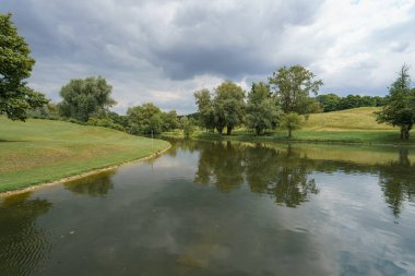 Sakin bir göl, sakin bir yaz gününde, yemyeşil yeşilliği ve etrafını çevreleyen ağaçları yansıtır. Doğa barışçıl güzelliğinin tadını çıkarıyor..
