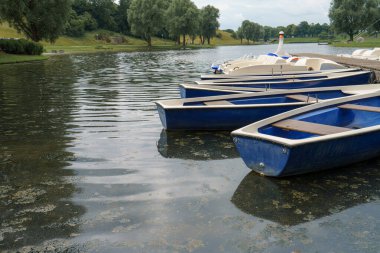Mavi kayıklar gölün berrak sularında huzur içinde yüzerek huzurlu bir atmosfer yaratırlar. Bereketli yeşil ağaçlar kıyı boyunca uzanır, güneşli bir günde huzuru yansıtır.