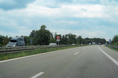 Araçlar, yeşil alanlarla çevrili iyi korunan bir otoyolda saatte 120 km hız sınırına işaret eden bir trafik levhası ile seyahat ediyorlar. Atmosfer sakin ve bulutlu, tipik bir mevsim..