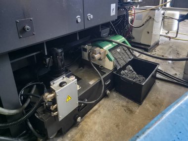 Bir endüstriyel atölyede, makineler çeşitli ekipmanlarla birlikte aktif olarak çalışır. Yoğun bir çalışma ortamı sergileyerek, zeminde düzenlenmiş malzeme ve araçlarla bakım devam ediyor.