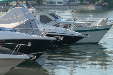 Gün ışığı suda parlarken birkaç tekne sakin bir marinada dinleniyor. Rüzgarda dalgalanan renkli bayraklar, canlı bir atmosfer yaratıyor. Gündüz oldu..