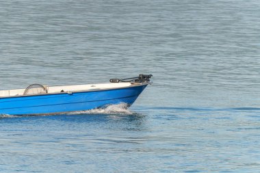 Küçük mavi bir tekne, güneş ışığını yansıtan sakin bir su kütlesi boyunca sorunsuzca hareket eder. Çevre sakin, sakin bir keşif için mükemmel..
