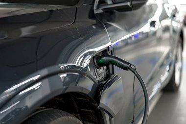 İyi aydınlatılmış bir otoparktaki şarj istasyonunda şık bir elektrikli araç şarj ediliyor. Yeşil şarj konnektörü görünür bir şekilde arabaya bağlı, sürdürülebilir teknoloji kullanımını vurguluyor.