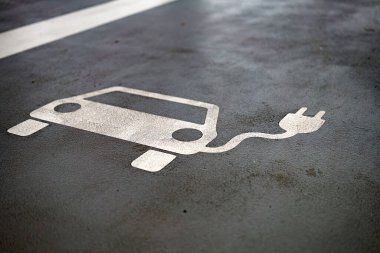 Beton bir yüzeyde elektrikli araç sembolü bulunan özel bir alan, gün içinde kentsel bir yerde elektrikli arabaları şarj etmek için bir alanı gösteriyor.