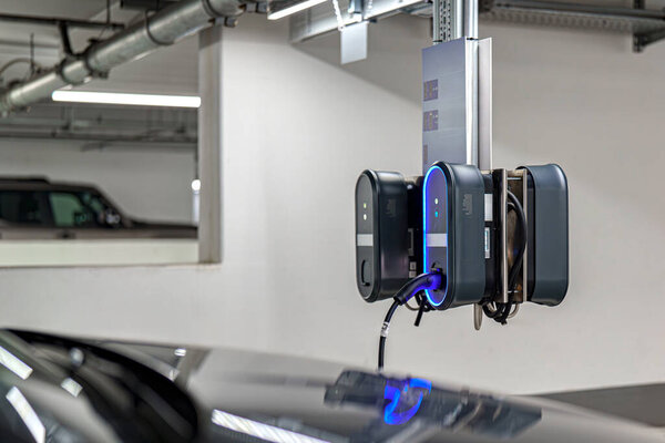 На стене в хорошо освещенном подземном гараже установлена электростанция зарядки автомобиля. Зарядные кабели висят вниз, готовые к использованию электромобилями.