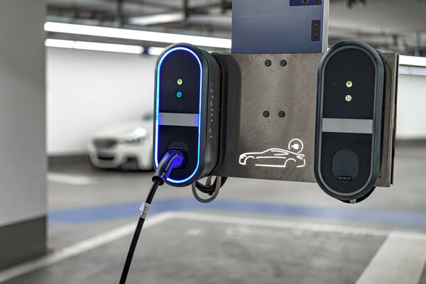Элегантная электростанция зарядки автомобилей расположена в хорошо освещенном подземном гараже. Два порта зарядки соединены кабелем зарядки, готовым к использованию.