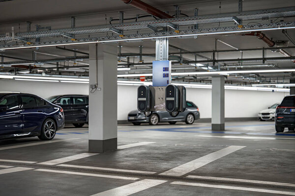 Зарядная станция для электромобилей видна на хорошо освещенной подземной автостоянке. Окружающие автомобили аккуратно припаркованы, демонстрируя современный дизайн и функциональность.
