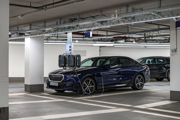 Гладкий электрический автомобиль подключается к зарядной станции в хорошо освещенном подземном гараже. Сцена запечатлевает чистые линии и современный дизайн, освещающий городскую жизнь.