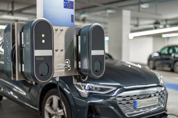 Станция зарядки для электромобилей расположена в современном гараже. Рядом припаркованы различные современные автомобили, демонстрирующие экологическую инициативу вождения.