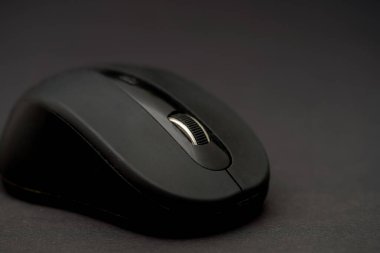 Pürüzsüz siyah bir bilgisayar faresi, tasarımı ve dokusunu sergileyerek karanlık bir arkaplanda dinlenir. Odak, zarif bir ayarda düğmelerini ve kaydırma çarkını vurgular.