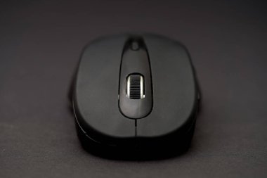 Siyah bir bilgisayar faresinin karanlık bir arkaplana yakın plan görüntüsü. Cihaz, ergonomik kullanım için ideal, belirgin bir kaydırma tekerleği ile pürüzsüz bir bitiş özelliğine sahiptir..