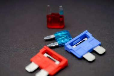 Koyu bir yüzeyde çoklu renkli elektrik sigortaları düzenlenmiştir. Kırmızı, mavi ve şeffaf bileşenler gösterilir. Devre koruma ve onarım için farklı dereceler gösterilir..