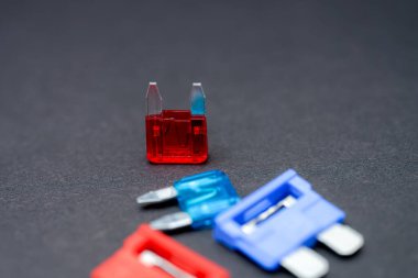 Farklı tipte otomotiv sigortaları karanlık bir yüzeye yerleştirilir. Canlı kırmızı fitil mavi ve turkuaz fünyelerin arasında duruyor, eşsiz tasarımlarını ve renklerini sergiliyor..