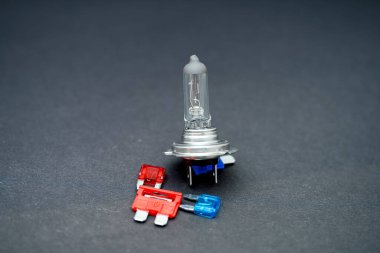 Bir araba ampulü belirgin bir şekilde metalik tabanı ve cam kapağı ile yakınlarda koyu bir arkaplan üzerine yerleştirilmiş kırmızı ve mavi fünyelerle yerleştirilmiştir..