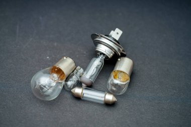 Bir grup farklı tip otomotiv ampulleri, eşsiz şekillerini ve cam tasarımlarını sergileyerek karanlık bir zemin üzerinde uzanır. Düzenleme, bunların işlevselliğini ve çeşitliliğini vurguluyor.