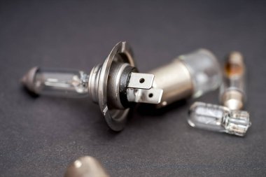 Değişik otomotiv ampulleri ve konnektörleri farklı şekil ve boyutlarda, karanlık bir yüzeye saçılmıştır. Odak, her bileşenin karmaşık ayrıntılarını ve işlevselliğini vurgular.