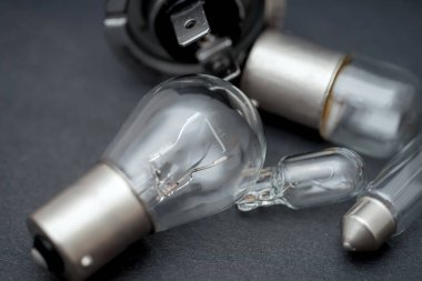 Farklı türde ampul ve otomotiv parçaları karanlık bir yüzeye yerleştirilir ve araç bakımına odaklanan bir atölyede çeşitli şekilleri ve bileşenleri gösterilir..