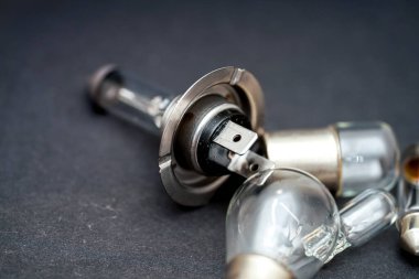 Karanlık bir yüzeye yerleştirilmiş, çeşitli şekil ve malzemelerin sergilendiği, otomotiv aydınlatmasında kullanılan karmaşık tasarım ve işçiliğin vurgulandığı bir araba farları koleksiyonu..