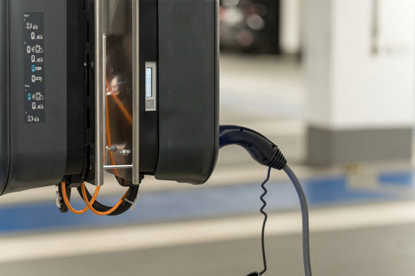 A charging station for electric vehicles is installed in a clean, well-lit parking garage. The connector is plugged in, ready to charge an electric car.