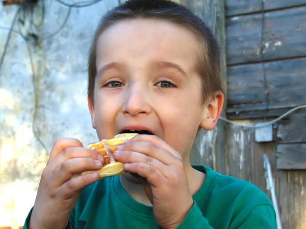stock image Boy eating a waffle on the background of the old house.