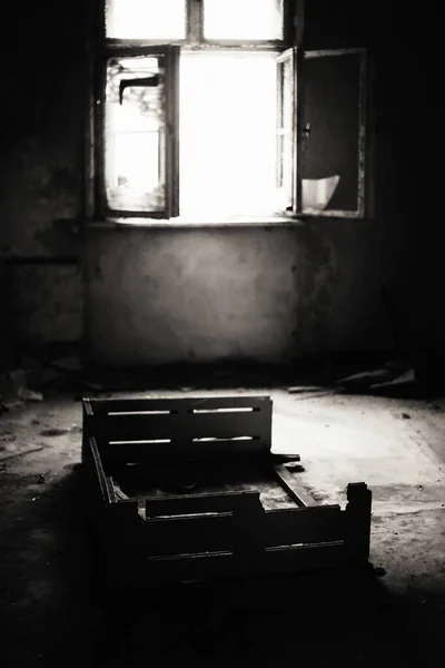 Small broken bed in a ruined room with backlight, black and white shot.